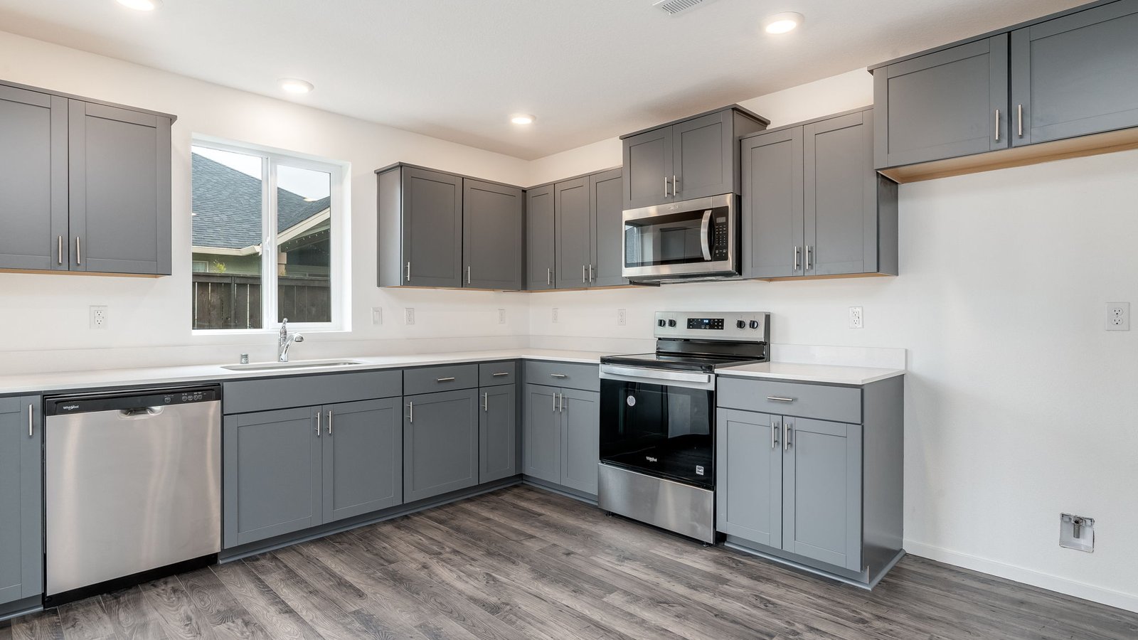 L-shaped kitchen with shaker cabinets, quartz counters, stainless steel appliances, and a pantry