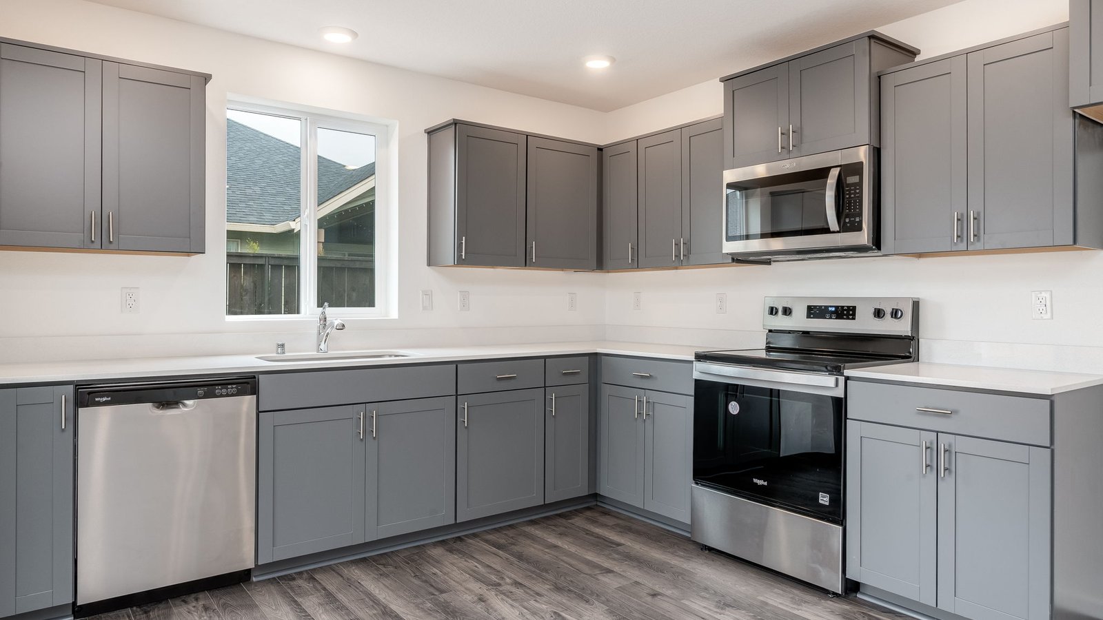 L-shaped kitchen with shaker cabinets, quartz counters, stainless steel appliances, and a pantry