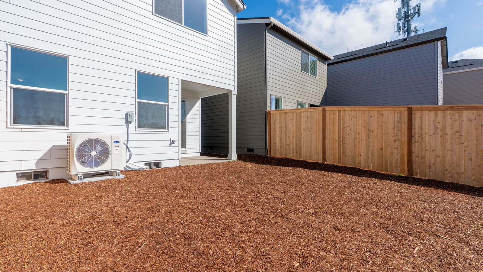 fully fenced backyard with bark chips and a patio