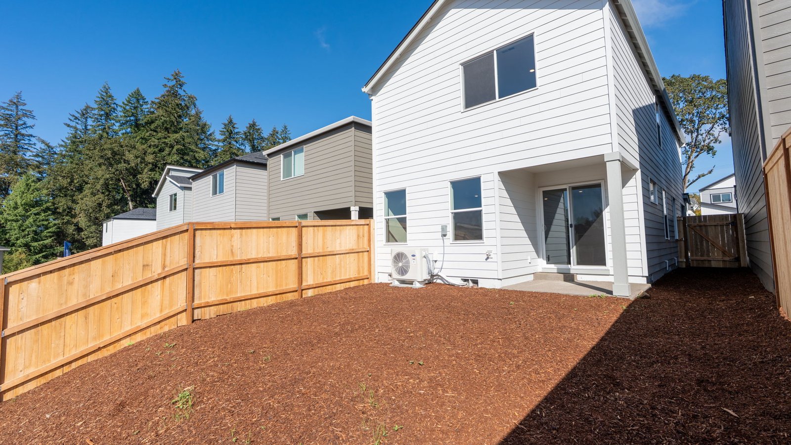 fully fenced backyard with bark chips and a patio