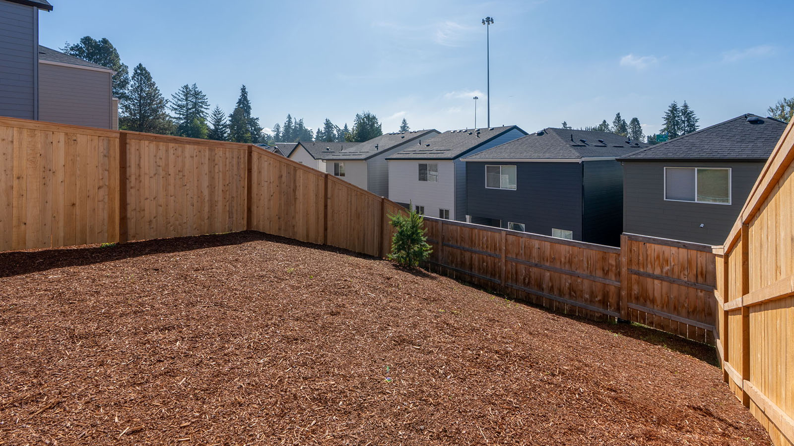 fully fenced backyard with bark chips and a patio