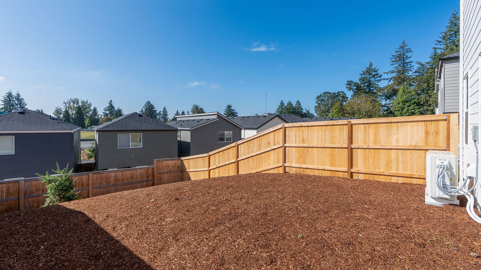 fully fenced backyard with bark chips and a patio