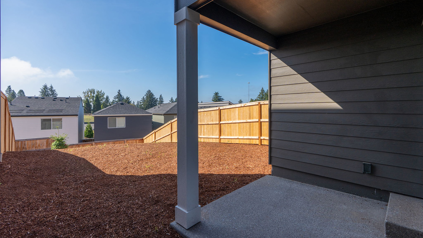 fully fenced backyard with bark chips and a patio