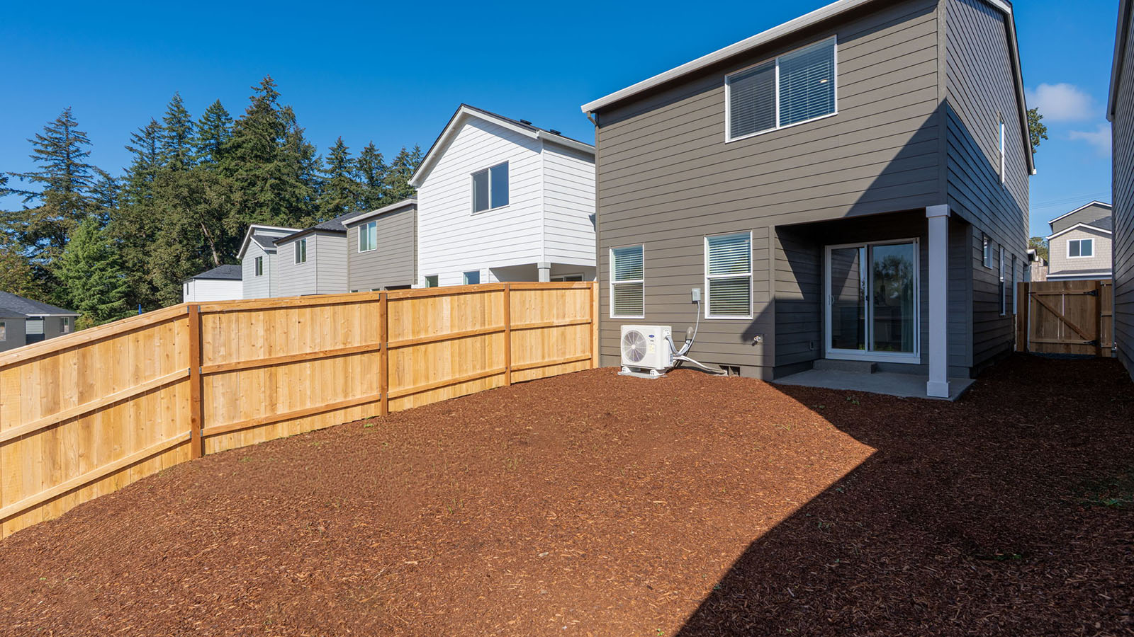 fully fenced backyard with bark chips and a patio