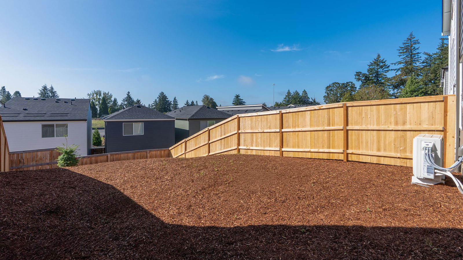 fully fenced backyard with bark chips and a patio