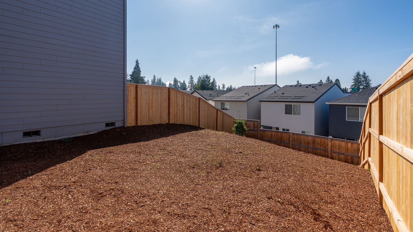 fully fenced backyard with bark chips and a patio