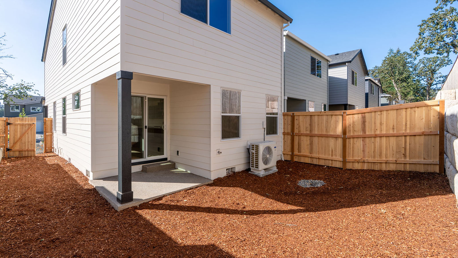 fully fenced backyard with bark chips and a patio