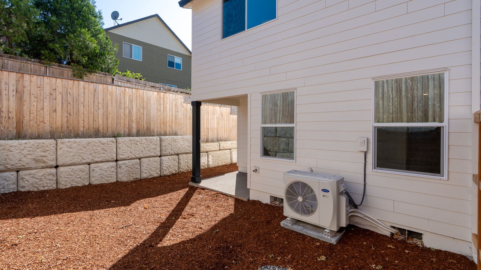 fully fenced backyard with bark chips and a patio