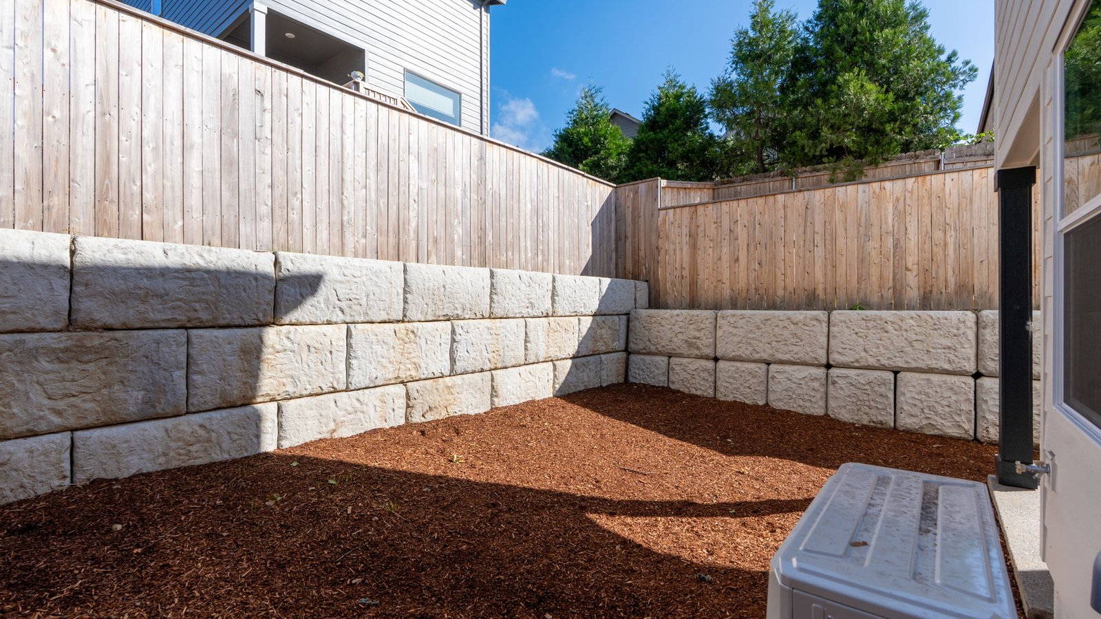 fully fenced backyard with bark chips and a patio