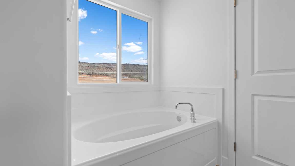 Large primary bathroom with quartz countertops, double sink vanity, and separate walk in shower and garden tub with window