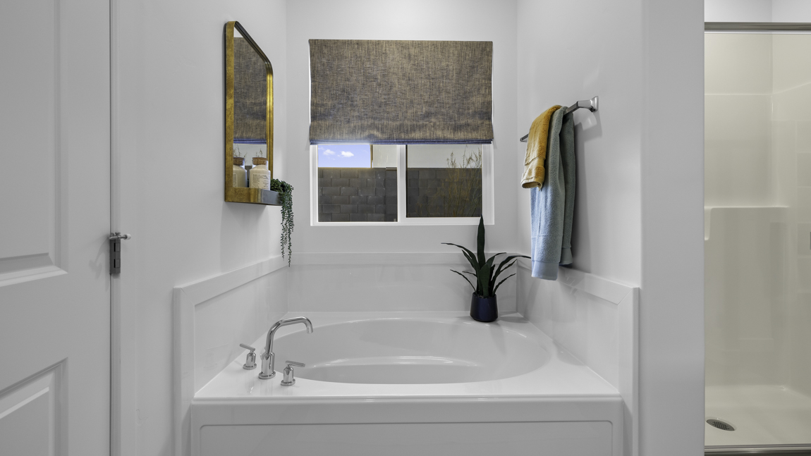 Large primary bathroom with quartz countertops, double sink vanity, and separate walk in shower and garden tub with window