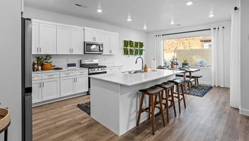 A wider view of the expansive kitchen and dining area with white cabinets and countertops with a large breakfast bar with sink, dining area and large window with a view to the back patio.