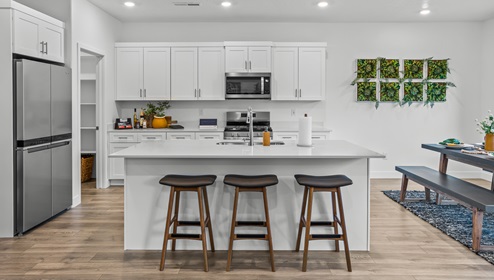 A full kitchen and pantry view of the Stillwater model home in the Long Valley community in Washington Utah, complete with white cabinets and white expansive countertops, stainless steel appliances and a large pantry.