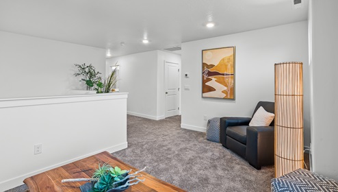 A view of the loft area with the half wall that overlooks the downstairs area and then view to the hallway to the other living spaces of the second level of the Stillwater model home.