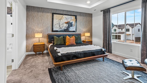 Primary bedroom with large bed, two side tables, a large window and sitting space across, complete with a recessed ceiling and canned lights and an ensuite full size bathroom.
