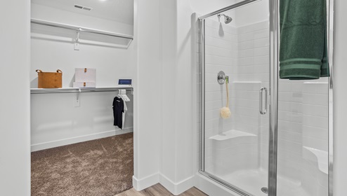 View of a portion of the large primary bedroom’s bathroom with a large standing glass enclosed shower and amazingly large walk in closet.
