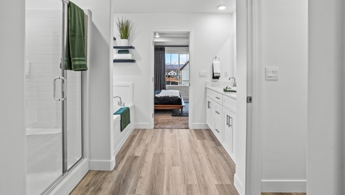 A view from the walk in closet past the expansive bathroom counter and double sink, free standing glass enclosed shower and tub nook with a window.