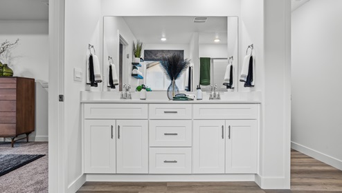 A bathroom sink with a lot of counterspace and white cabinets and expansive mirror.