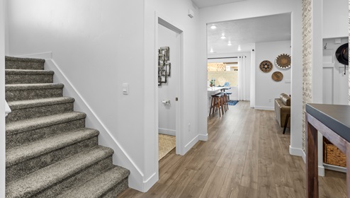 Entryway into the open concept Stillwater model home with a wide plush carpeted staircase and view into the mudroom, convenient powder room and then main living area at the Long Valley master planned community in Washington Utah.