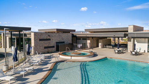 Long Valley clubhouse in the pool and hot tub area lined with lounge chairs and blue umbrellas.