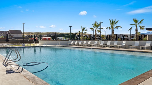 View of the large community pool where a long line of lounge chairs and palm trees beg you to sit and relax poolside at the Long Valley new home community in Washington Utah.
