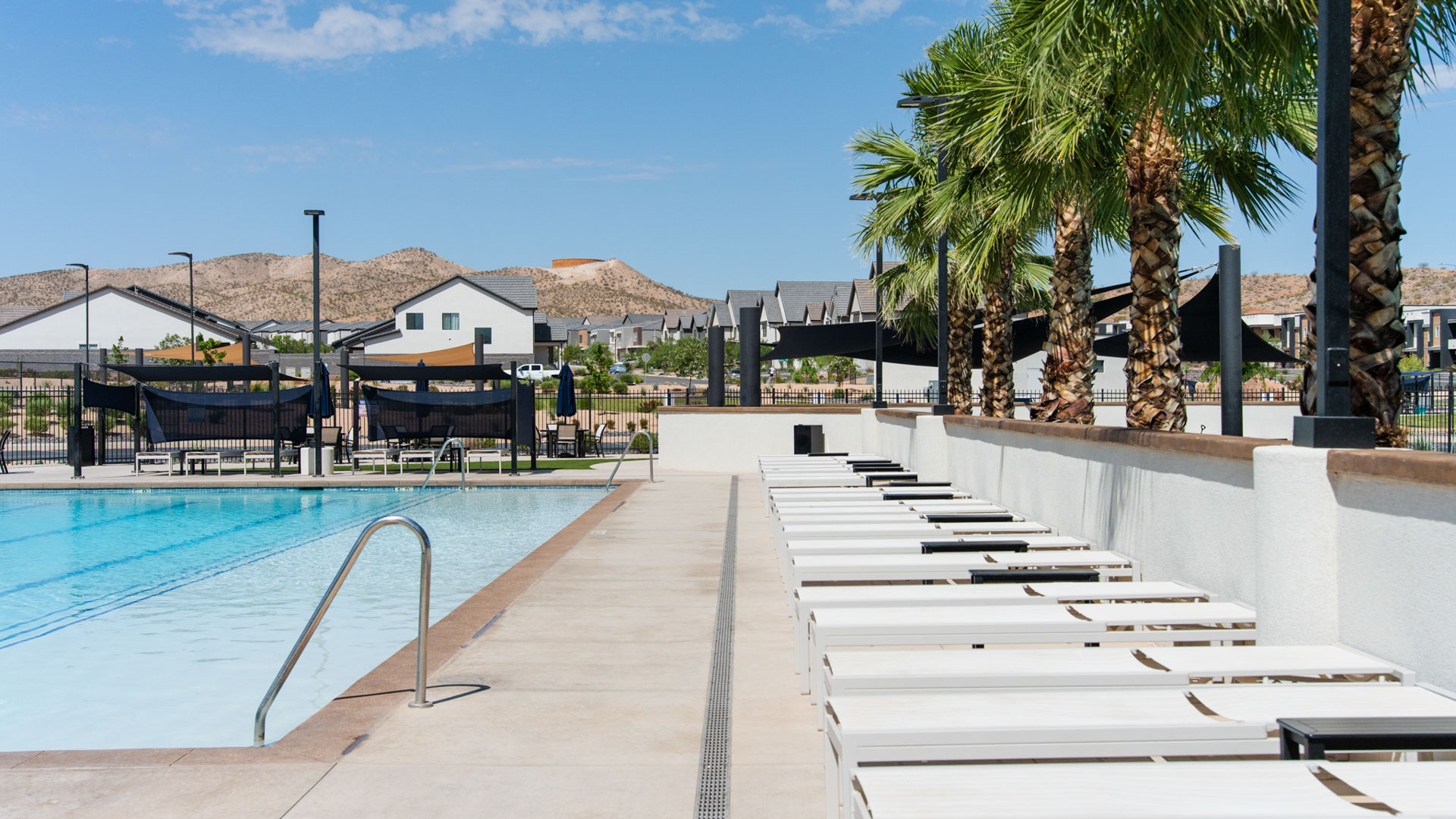 Another view of the pool lined with lounge chairs, umbrellas and palm trees.
