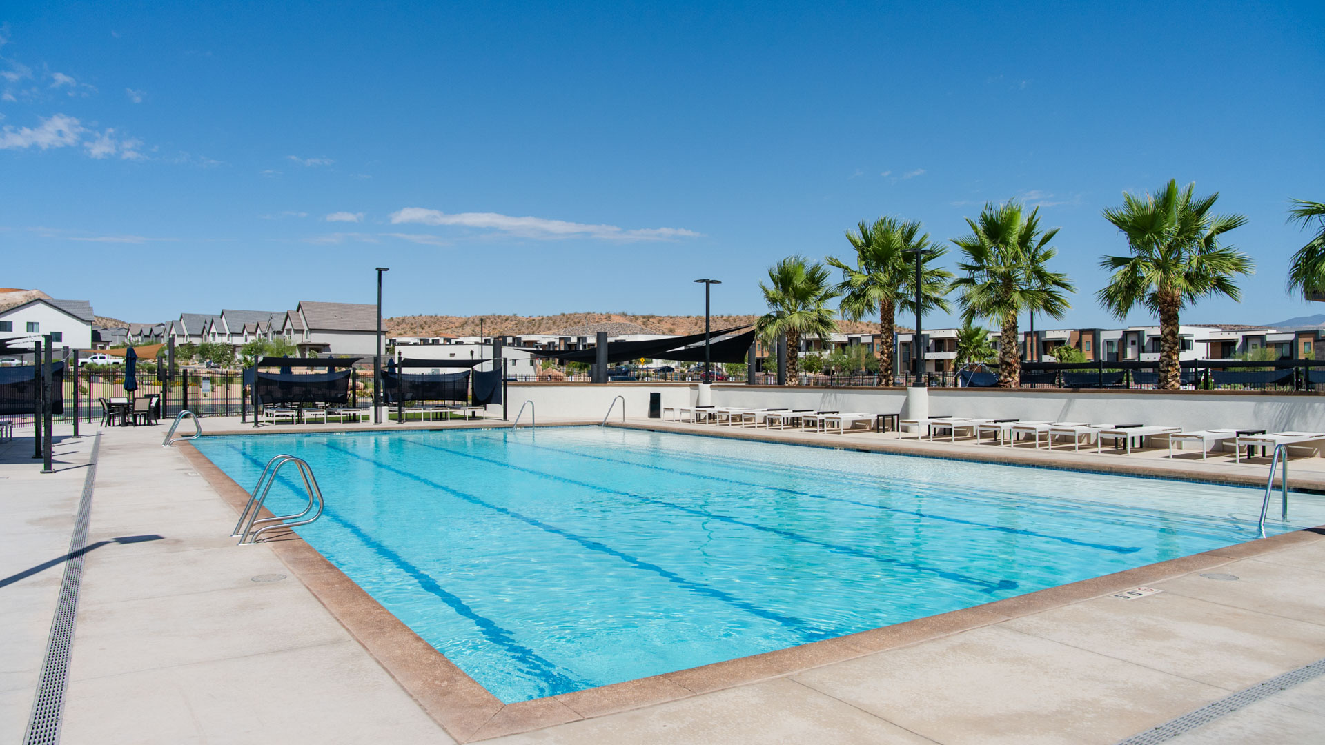 View of the large community pool where a long line of lounge chairs and palm trees beg you to sit and relax poolside at the Long Valley new home community in Washington Utah.