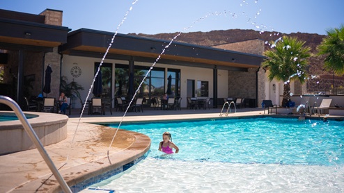 View of the large community pool where a long line of lounge chairs and palm trees beg you to sit and relax poolside at the Long Valley new home community in Washington Utah.