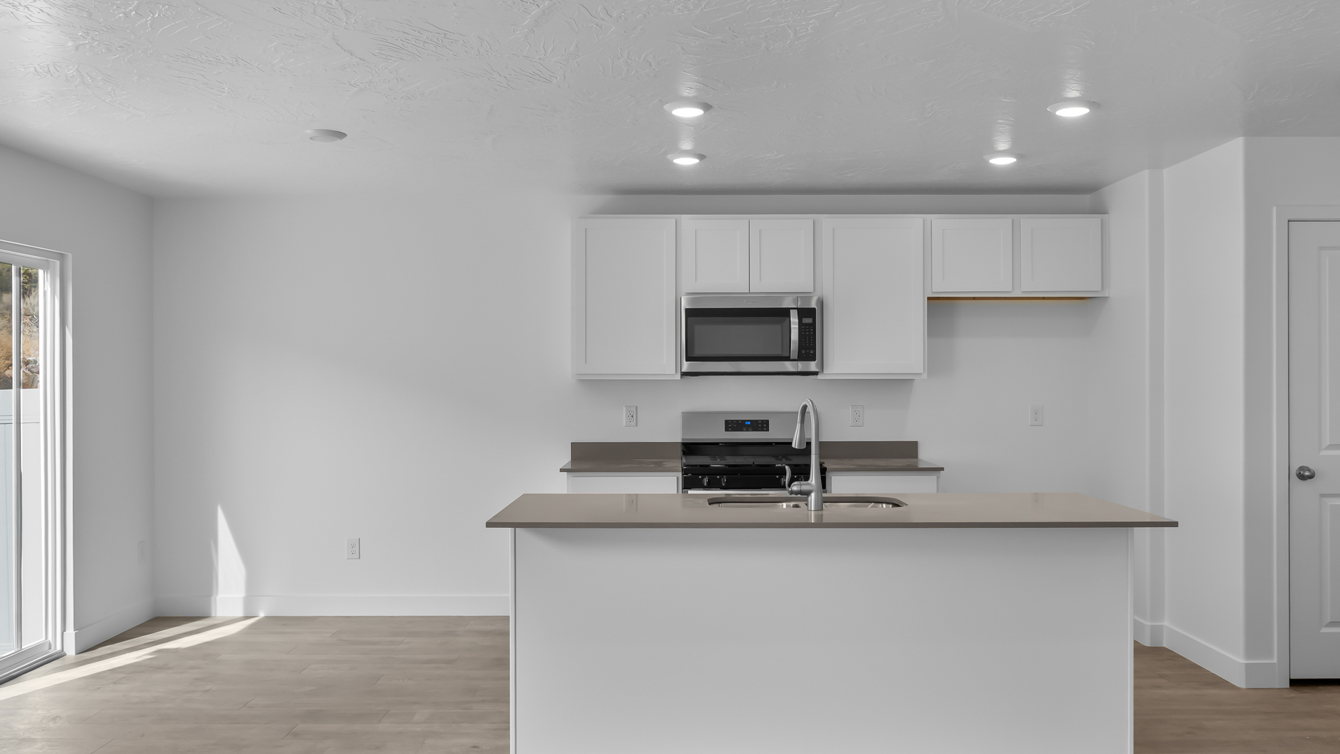 Kitchen space with island featuring white cabinets and gray countertops and showcasing dining space with patio doors.