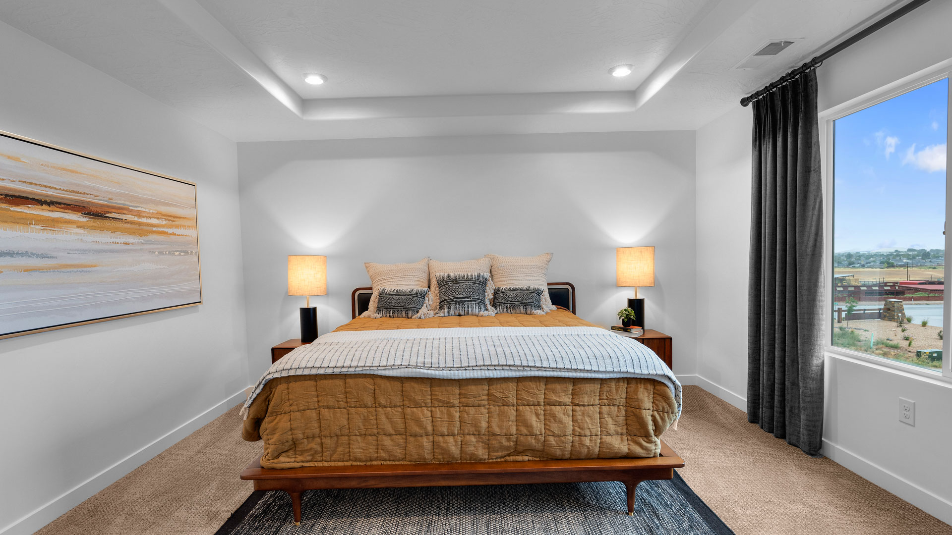 Primary bedroom with tray ceiling and large window.