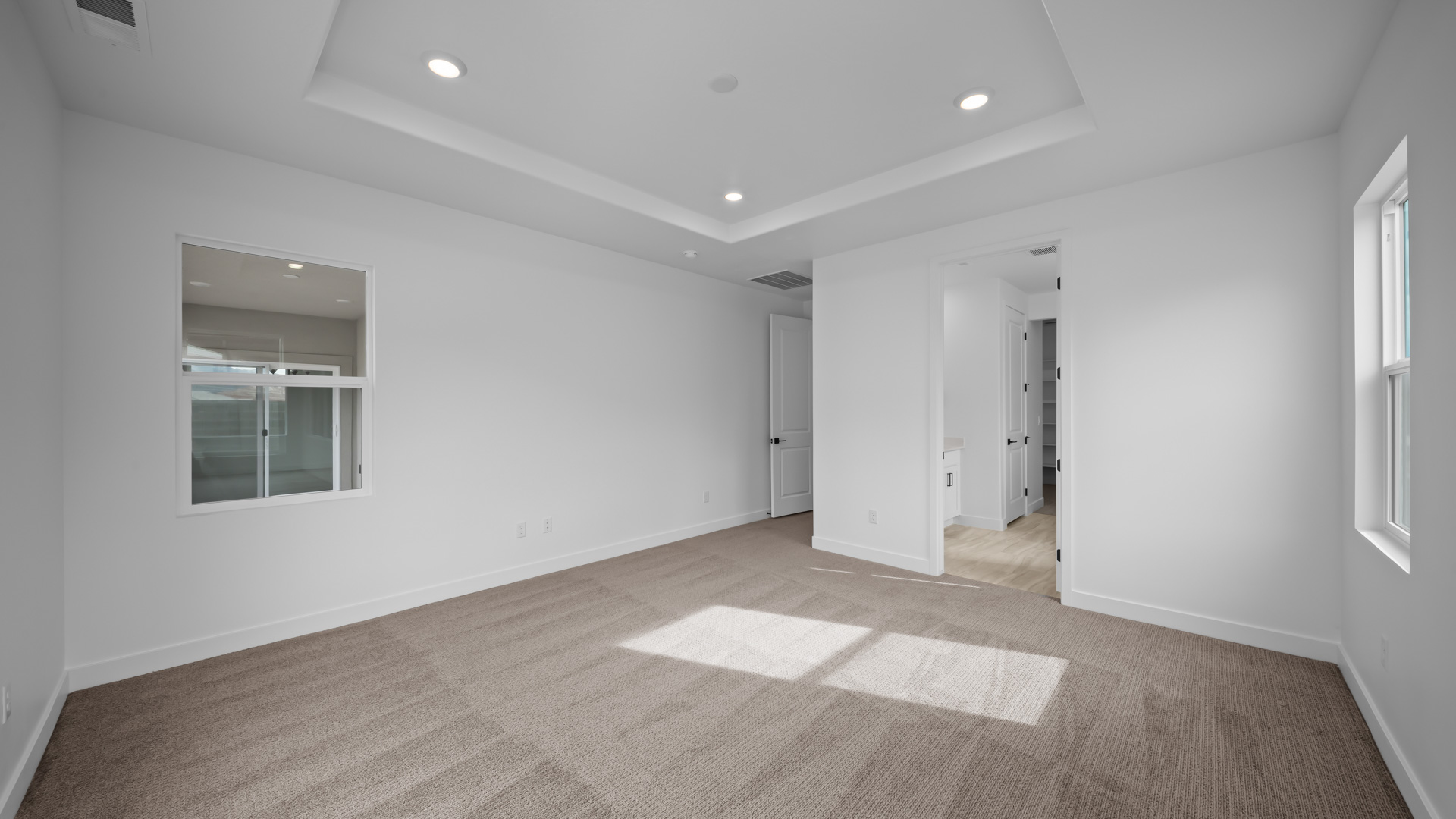 Primary bedroom with tray ceiling and windows.