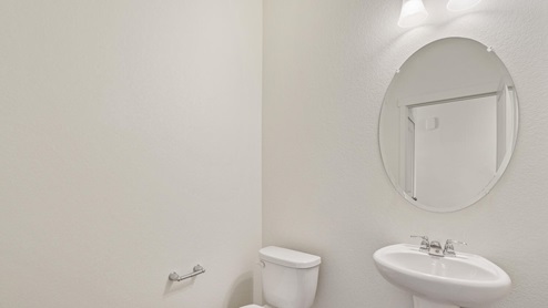 half bath with a round mirror, sink, and toilet