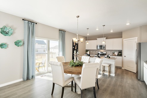 Open floor plan conjoining contemporary kitchen and dining area with a thick round wooden table and sliding glass door.