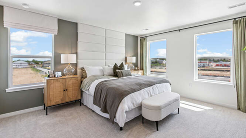 Melbourne model home primary bedroom with modern wood furniture, window drapes flanking 3 large operable windows