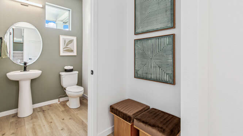 Modern powder room of furnished Melbourne model home featuring a pedestal sink, oval mirror, LED light fixture and clerestory window. Nook upon entry.