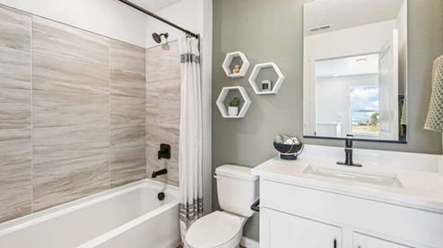 Secondary bathroom in furnished Melbourne model home displaying a quartz countertop vanity with dual undermount sink and tub/shower combo