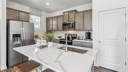 Muirfield furnished model kitchen with quartz countertop island, contemporary cabinetry, and stainless-steel appliances