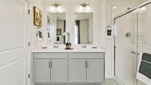 gray cabinet bathroom with a shower and two undermont sinkd