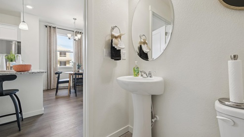 half bath with a round mirror, sink and toilet