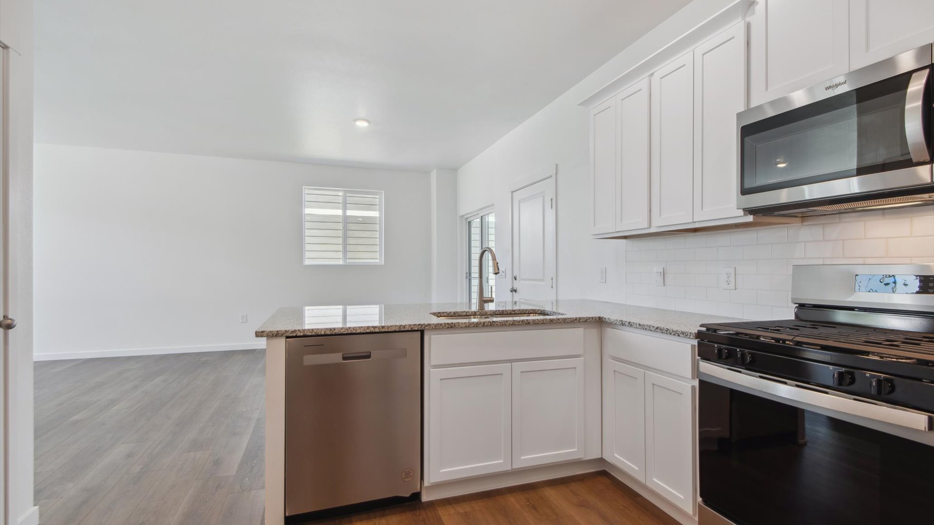 Douglas kitchen peninsula with stainless steel dishwasher, oven and microwave, white cabinetry and full-height backsplash