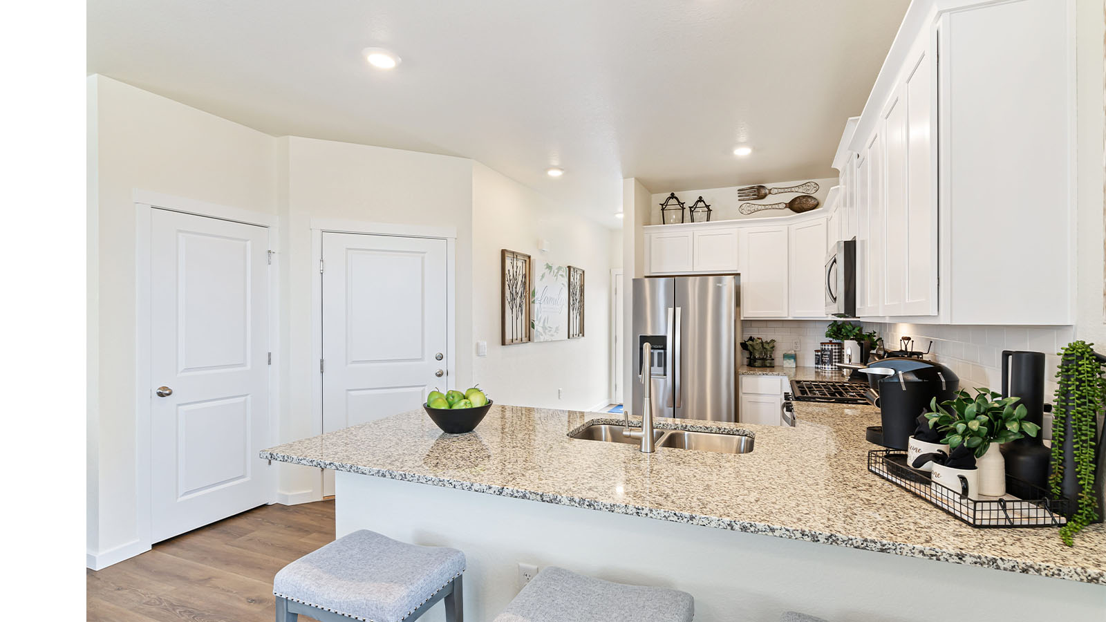 Alt angle view of Alamosa plan kitchen showing peninsula with undermount sink, seating and doors to garage and storage closet