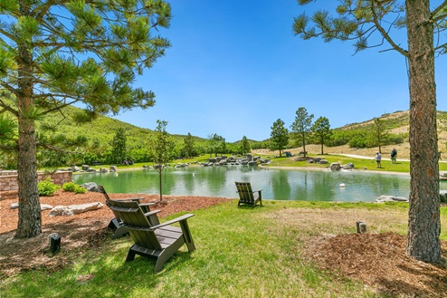 Adirondack chairs facing pond and waterfall located at golf course in Castle Rock Colorado with territorial views and golfers