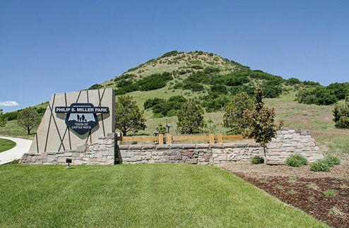 Stone, concrete, and wood accent monument for Philip S. Miller Park with lawn and walking path, and large hill behind