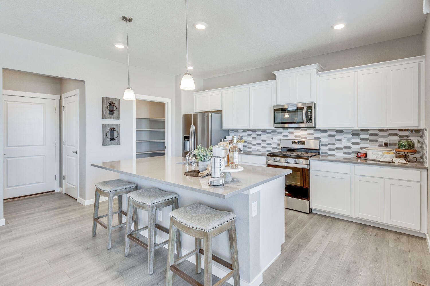 Kitchen staged with stools below island with overhang, and walk-in pantry in background