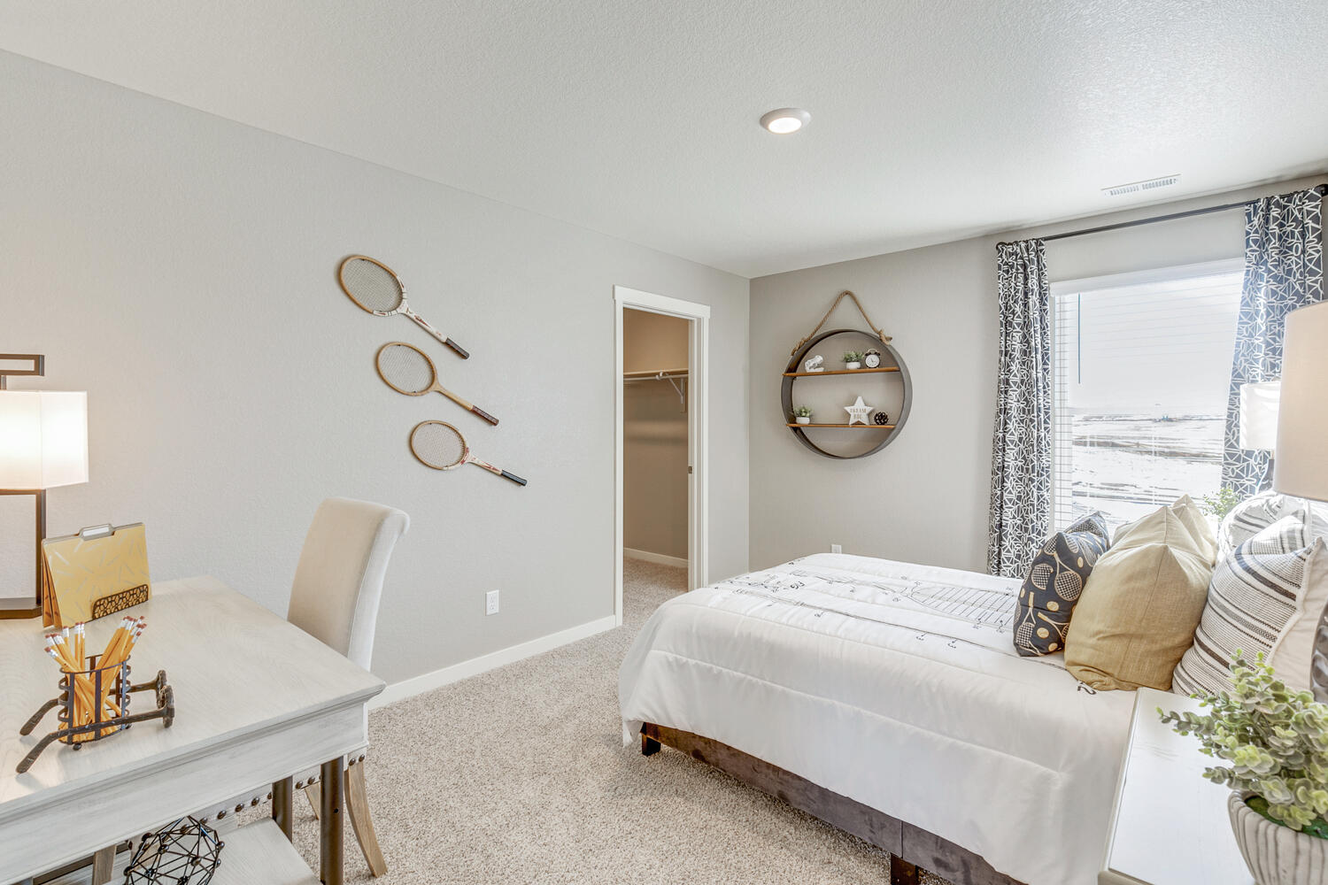 Secondary bedroom staged with desk and twin bed, featuring walk-in closet