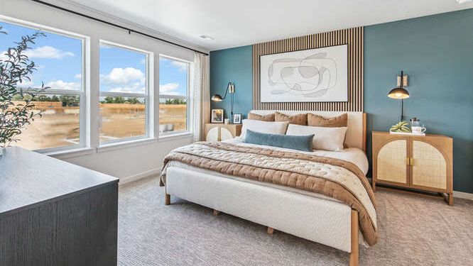 Muirfield model home primary bedroom with modern wood furniture, window drapes flanking 3 large operable windows