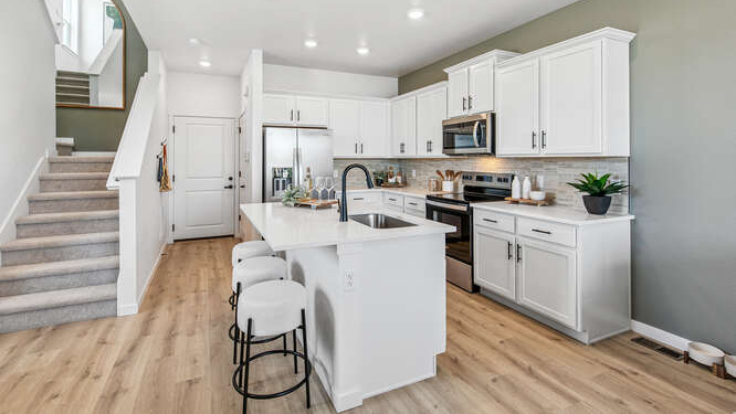 Wide angle of kitchen of Melbourne model home with bright modern LED light fixtures and background stairwell and garage door entry