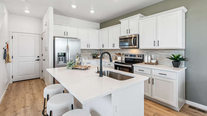 Wide interior view of Melbourne model home kitchen with central island and sink at left and ample storage cabinets throughout