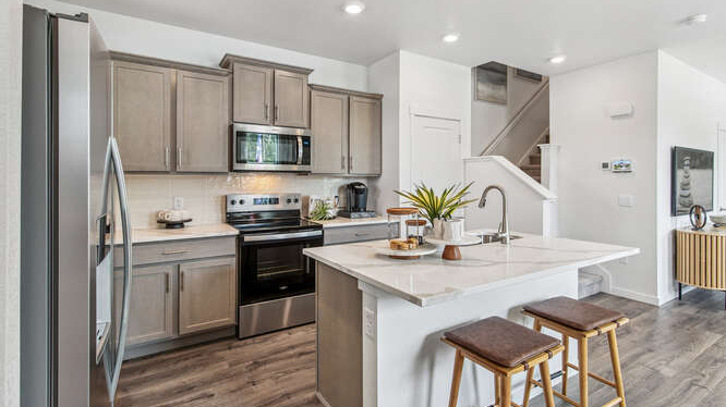 Model home kitchen located just inside the entry door with central island with dining space adjacent and living room beyond