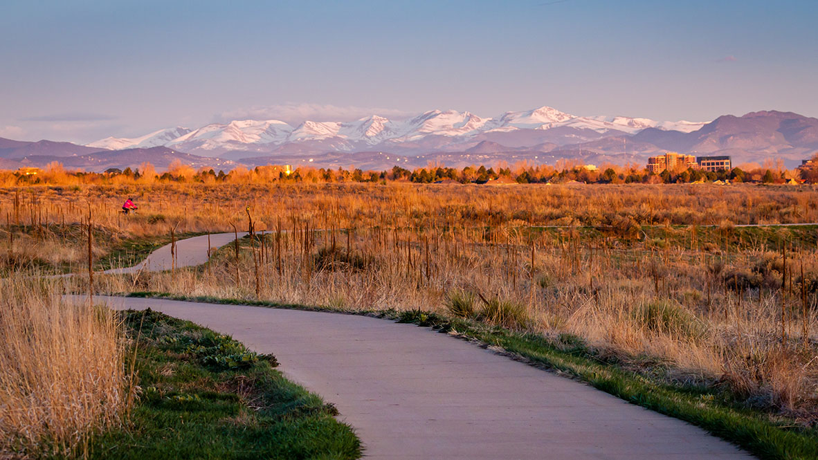 A walking path through Cherry Creek State Park at dusk with a view of the Rocky Mountains in the background.